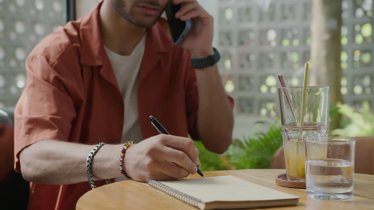 Man Taking Notes during Phone Conversation in Cafe