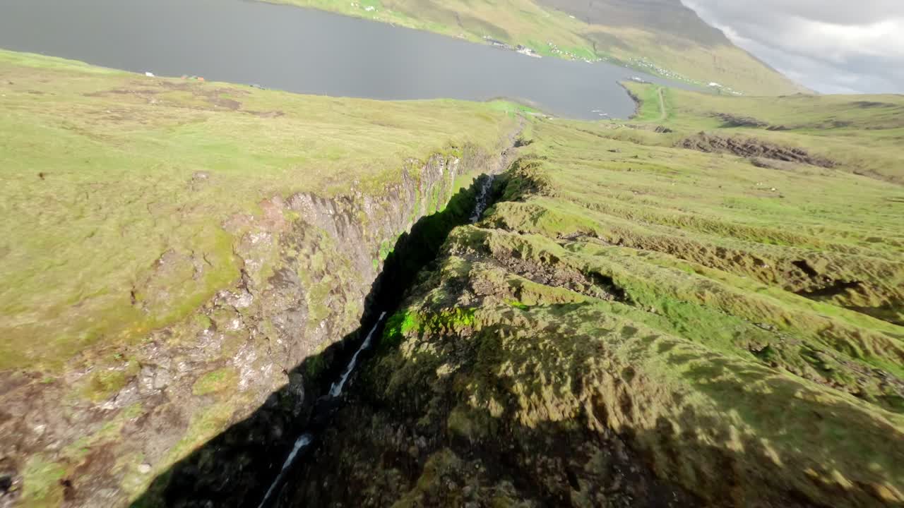 Steep grassy cliffs in the faroe islands with a serene fjord below, aerial view