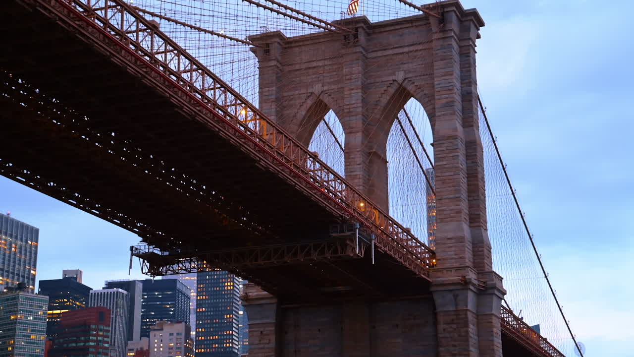 Close-up of the Brooklyn Bridge tower at dusk. The Brooklyn Bridge tower stands tall with the city lights of Manhattan glowing in the background