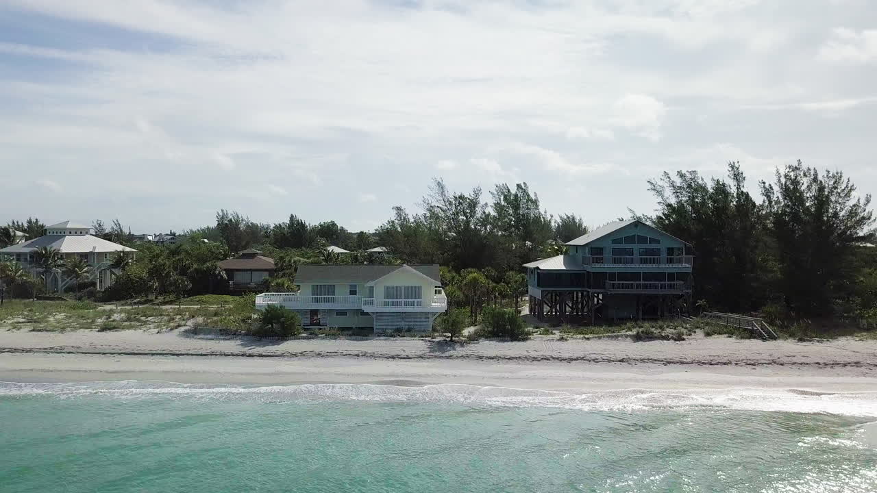 High to low drone flight from private beach housing community to reveal two houses on beachfront property with waves crashing on shore