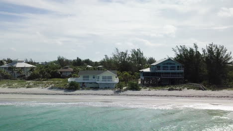 high to low drone flight from private beach housing community to reveal two houses on beachfront property with waves crashing on shore