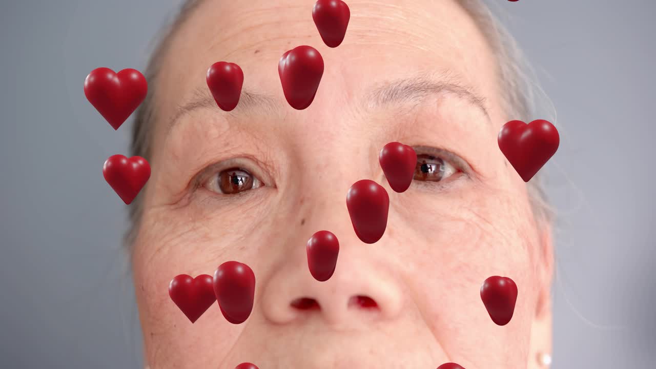 Senior woman shifting gaze, blinking; red 3D hearts appearing, drifting, following face for health