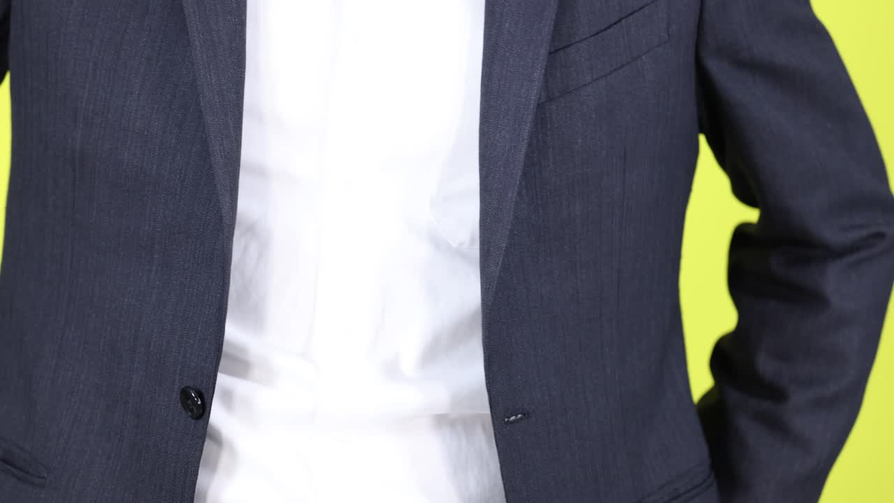 Professional man in suit adjusts jacket, standing against bright yellow background, medium close-up shot