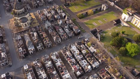 Small-Car-driving-on-road-at-Chacarita-Cemetery-Buenos-Aires-during-sunlight---Drone-top-down-shot-of-church-and-gravestones