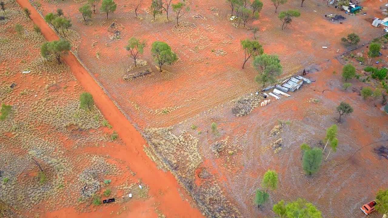 The Central Australian Outback. Cinematic aerial dolly forwards with a tilt up, to reveal rural settlements and a low mountain range. Filmed on a DJI Mavic Pro on a Camel Farm near Alice Springs.