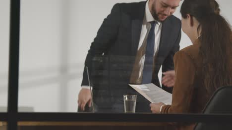 male candidate being interviewed in office for job by female interviewer viewed through window 5