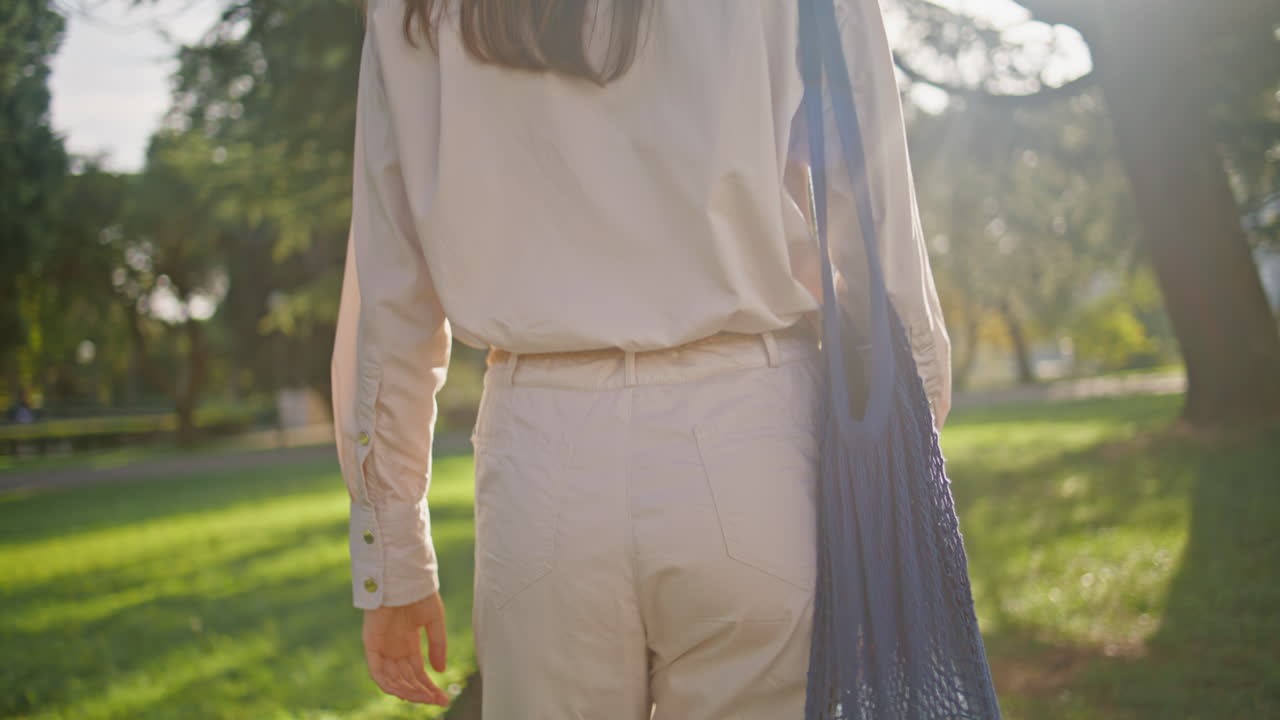mujer ecológica paseando por el parque vista trasera de primer plano. niña caminando con bolsa