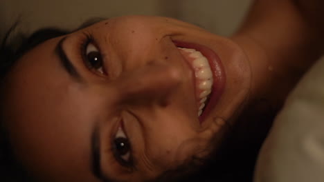 mujer joven en la cama temprano en la mañana con una gran sonrisa feliz y ojos marrones brillantes - cerrar