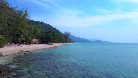 koh chang island, thailand showing a beautiful tropical white sand beach and lush rainforest meeting turquoise water. lovely aerial view static tripod hovering drone