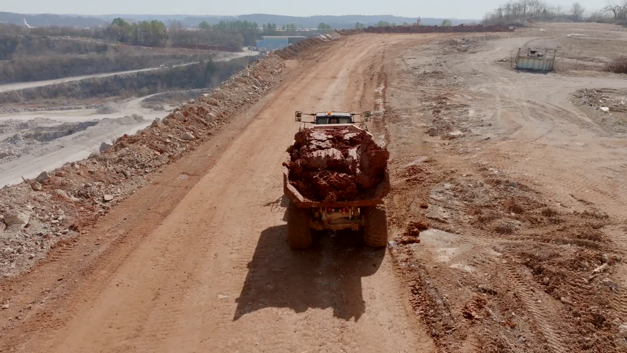 Aerial footage following a construction dump truck full of clay driving up a hill.