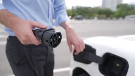 el hombre de negocios conecta el enchufe del cargador progresivo de la estación de carga a su ev.