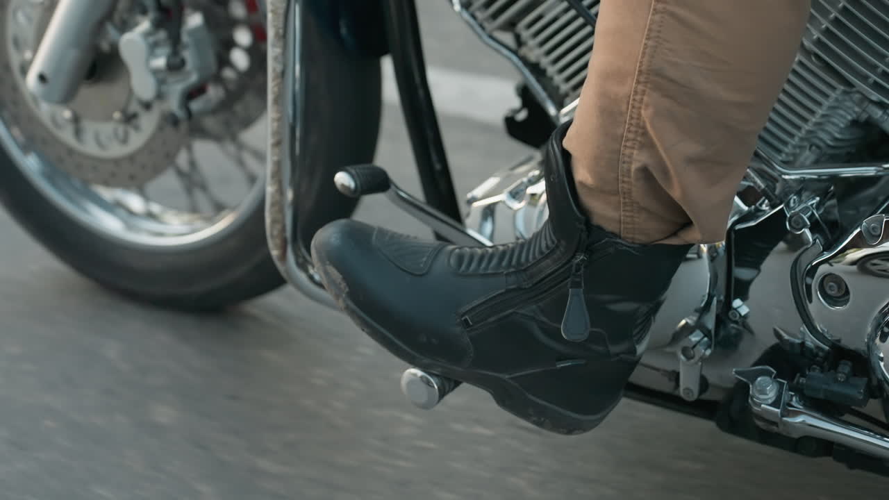 Lower angle view of motorcycle in motion highlighting rider boot on footrest, chrome engine details, and gear shifter against blurred asphalt road, capturing and speed