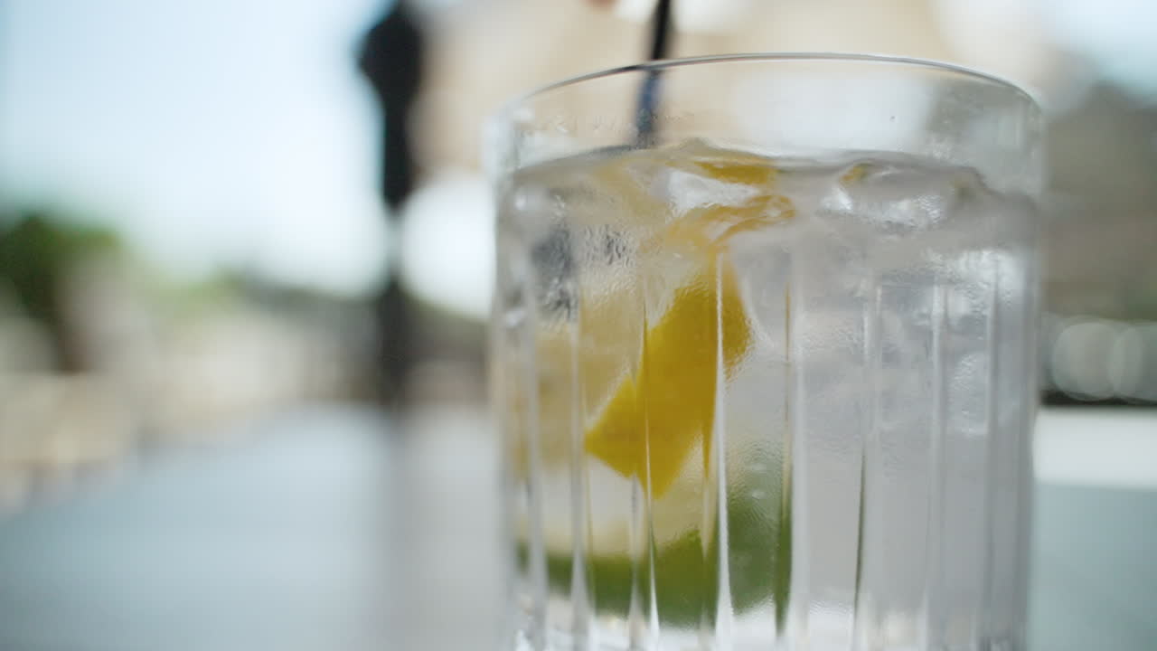 Primo piano di una cannuccia che mescola acqua, cubetti di ghiaccio, limone e lime in un bicchiere trasparente