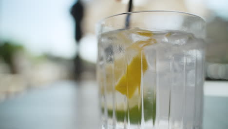 close up of straw mixing water, ice cubes, lemon and lime in a clear glass