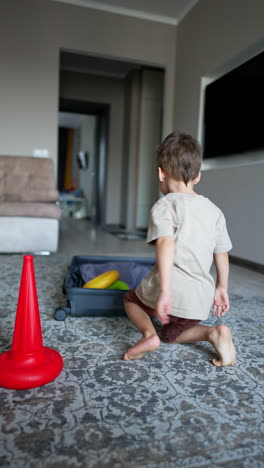 rear view of a kid sitting near toy pyramid. toddler puts the toy details into the opened suitcase. vertical video.