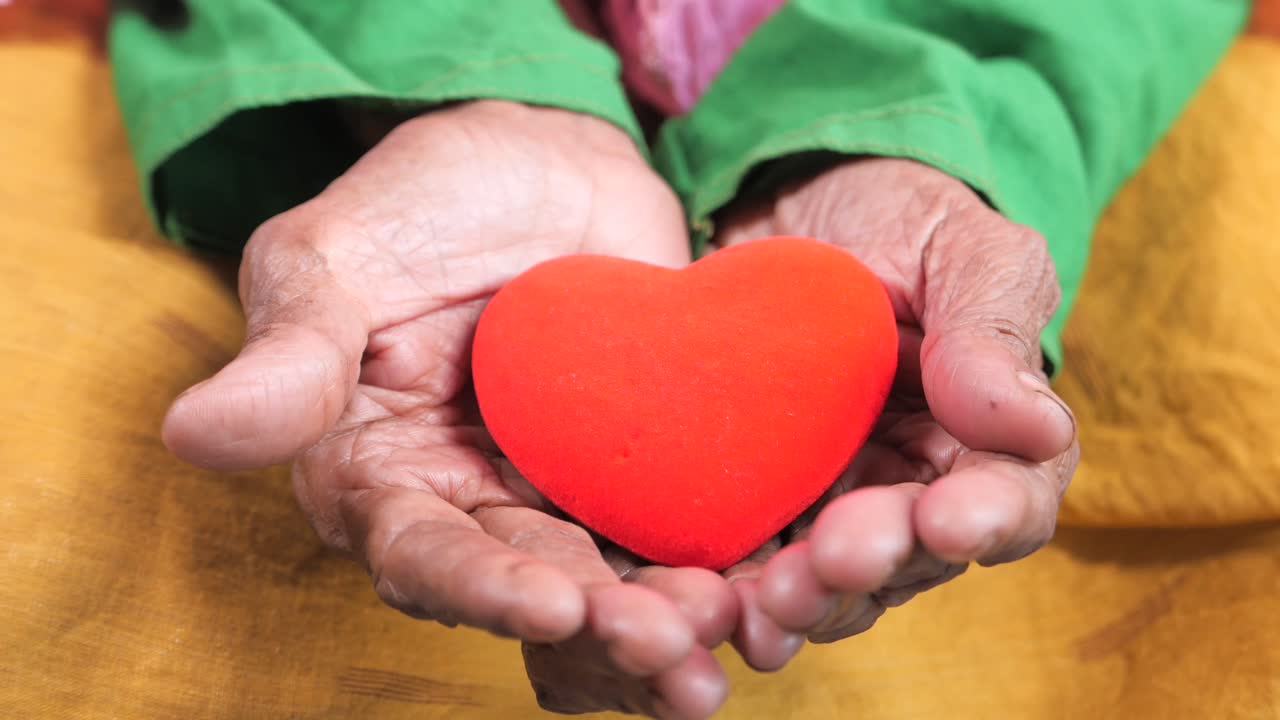manos de ancianos sosteniendo un corazón rojo