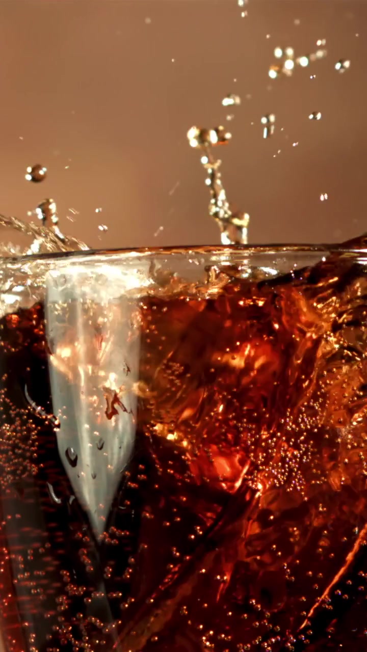 Cámara lenta de cubitos de hielo salpicando en un vaso de cola