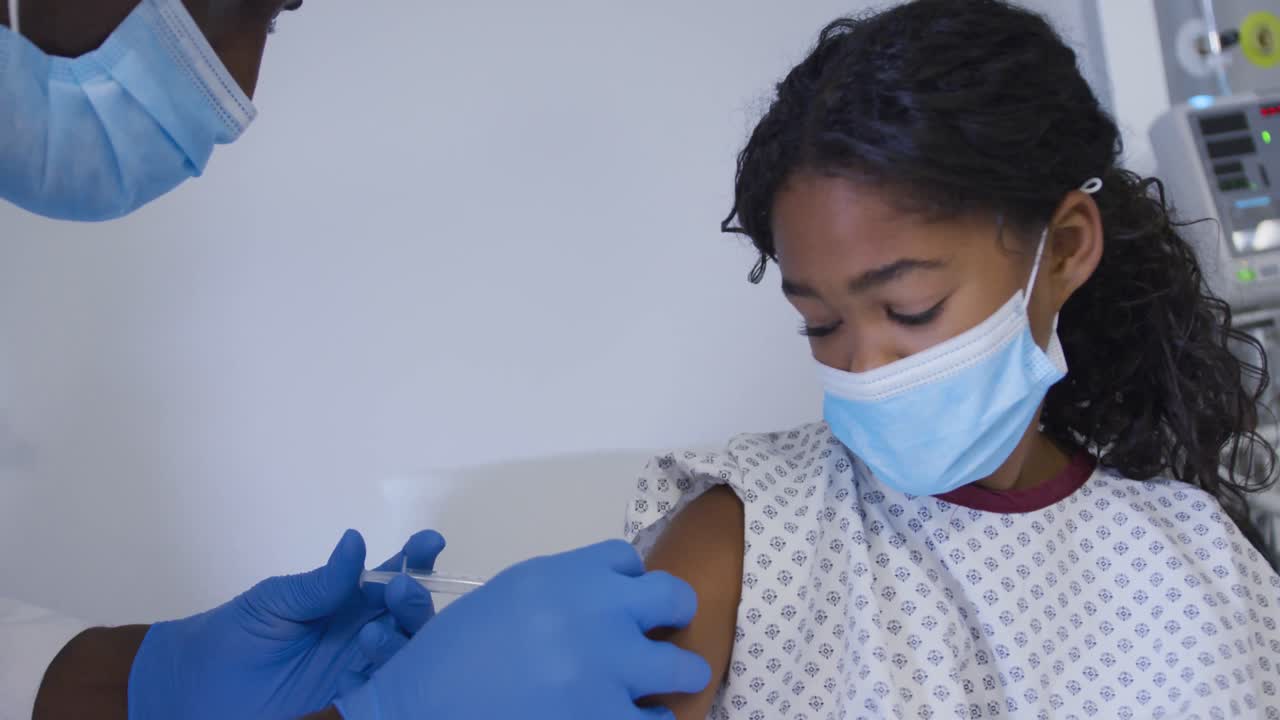 Afroamerikansk seniorlæge, der giver en pige covid-19-vaccine på hospitalet.