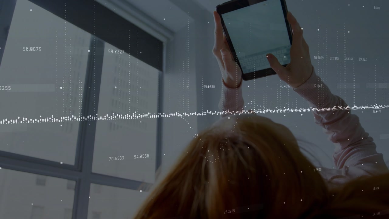 Woman lifting tablet and tapping while transparent waveform overlay animating live tech data feed