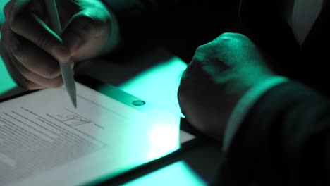 electronic signature with green light. businessman signing a business contract with stylus pen on tablet at night. man signing contract on tablet at office. business and technology concept.