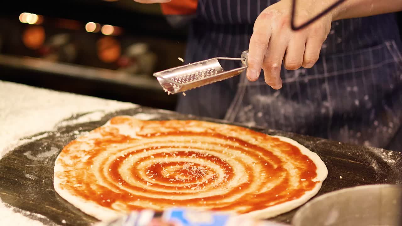 Chef grates cheese over pizza dough