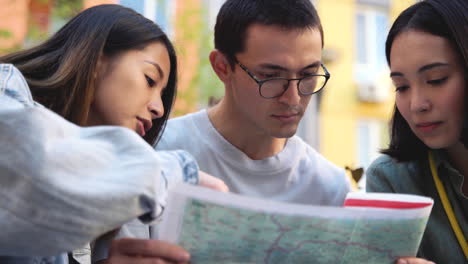 group of three young japanese friends looking together at map outdoors in the park