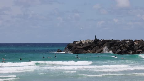 surfers riding waves near a rocky outcrop