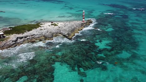 punta cancun lighthouse on rocky cliff surrounded by transparent waters, mexico. aerial drone descending
