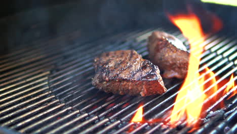 steaks grilling over the open flame of a backyard barbecue in slow motion