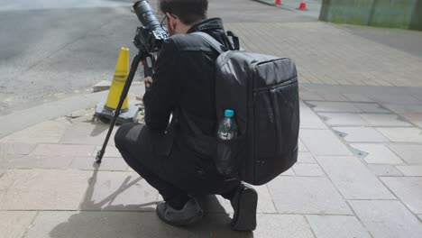 Closeup-videographer-using-camera-and-tripod-with-camera-bag-on-his-back