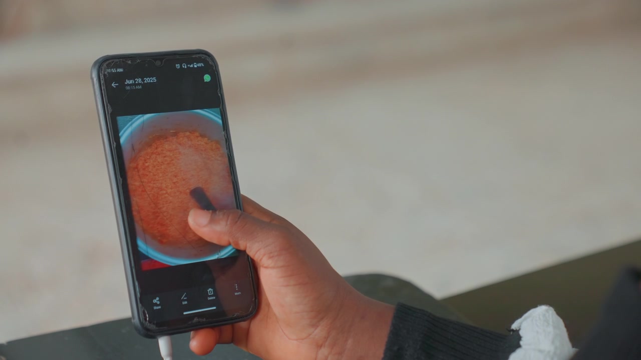 Mãe inspecionando foto de lanche crocante no telefone, mãe negra toca a ponta do dedo na tela sensível ao toque, close-up da mão sobre a imagem de um prato, ambiente de cozinha doméstica e planejamento tranquilo de refeição para a criança.