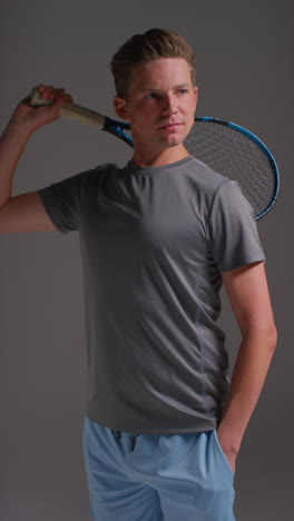 vertical video studio portrait of male tennis player holding racket shot against grey background