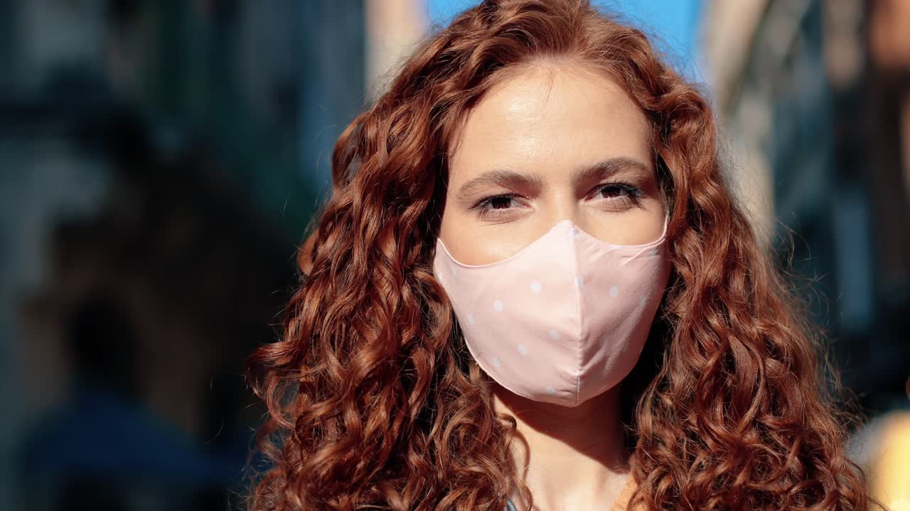 카메라를 보고 거리에서 웃는 마스크를 쓰고 빨간 머리 여자의 클로즈업 보기