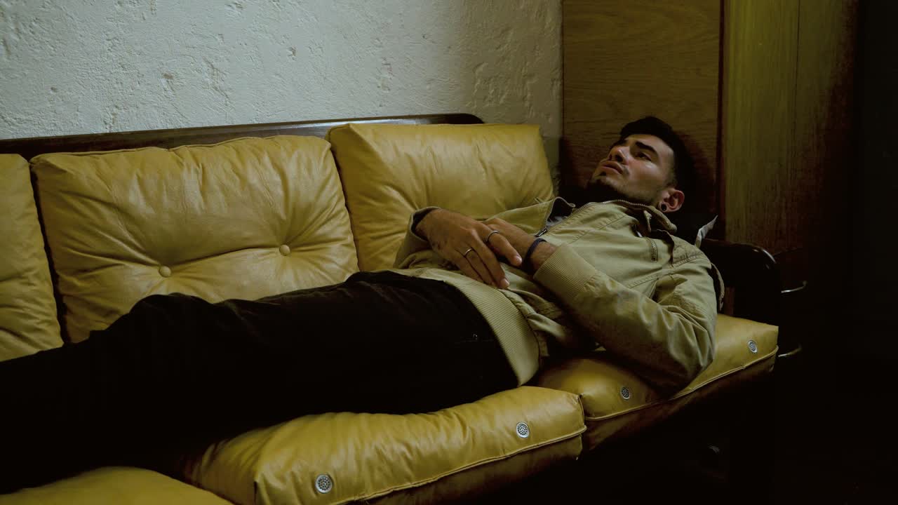 Anxious young man lying on a vintage leather sofa, gesturing and expressing distress. He is going through a difficult emotional period