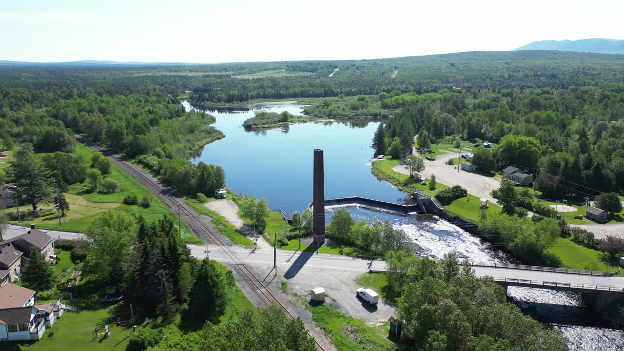 Aerial View of a Rural Landscape with Lake, Dam, Railroad Tracks, and a Tall Chimney