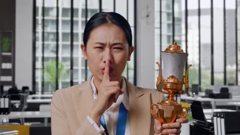 businesswoman holding a trophy with a shhh gesture