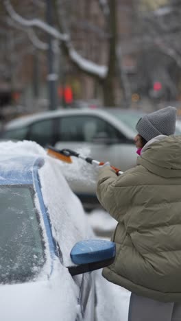 woman removing snow from car in snowy city