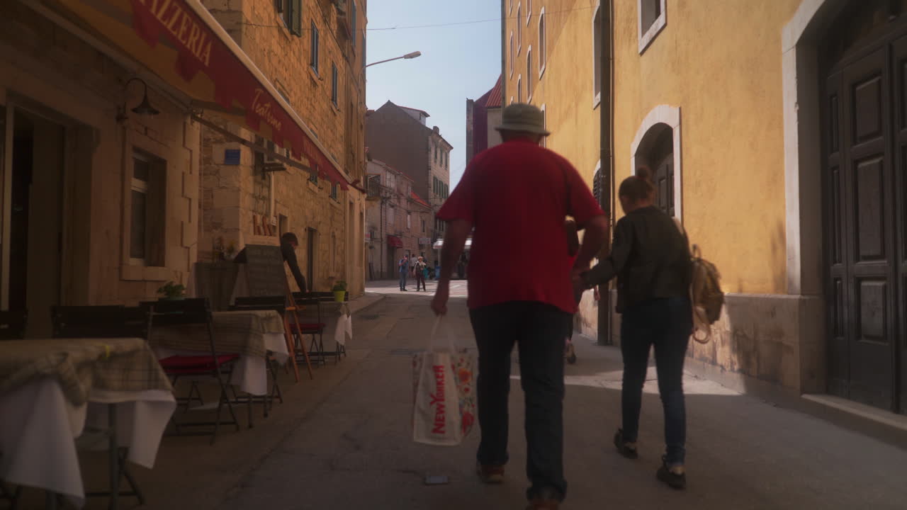 People walking on a narrow street with buildings and outdoor cafes in an old European town
