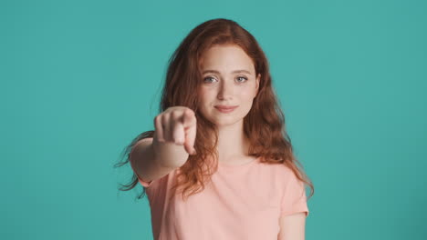 una chica pelirroja nerviosa frente a la cámara sobre un fondo turquesa.