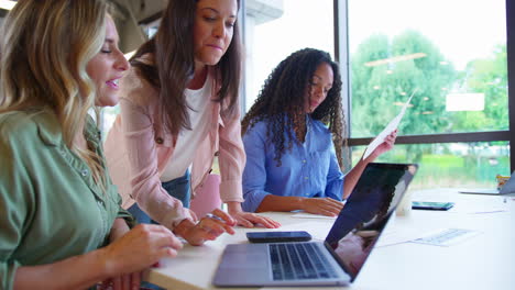 equipo de negocios femenino multicultural sentado en un escritorio con una computadora portátil en la oficina colaborando en un proyecto