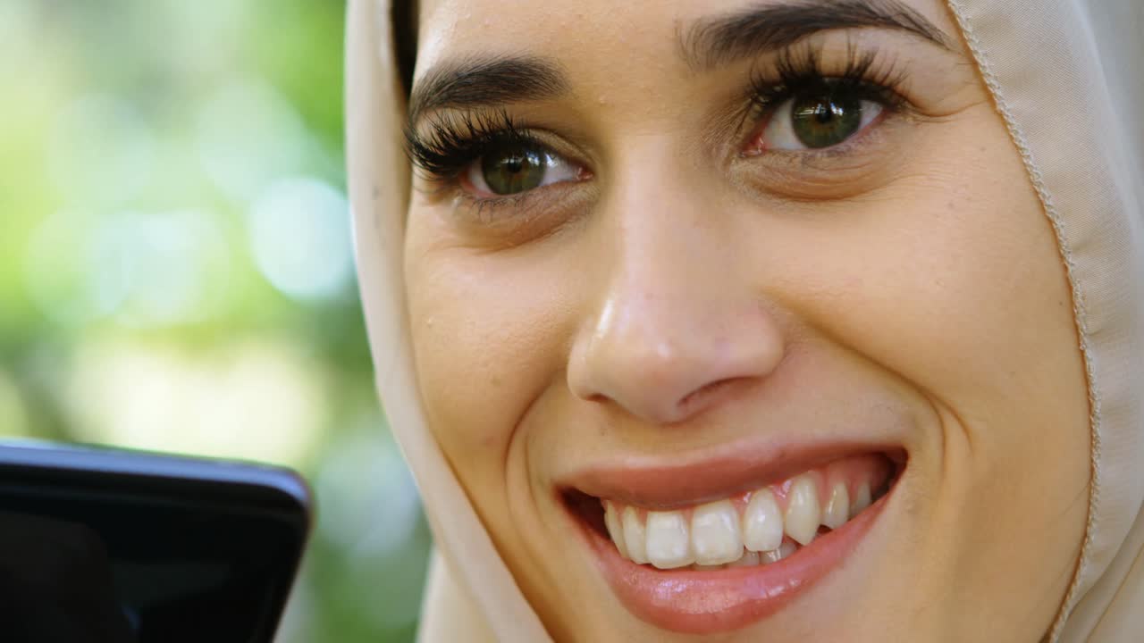 mujer en hijab sonriendo mientras usa teléfono móvil 4k