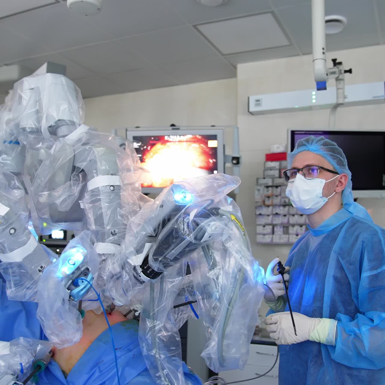 Young male doctor in mask and glasses holding an instrument in hand. Surgeon stands by futuristic equipment looking how it works