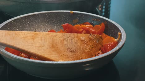 el vapor sale de una sartén al cocinar pimientos y zanahorias con una espátula de madera.