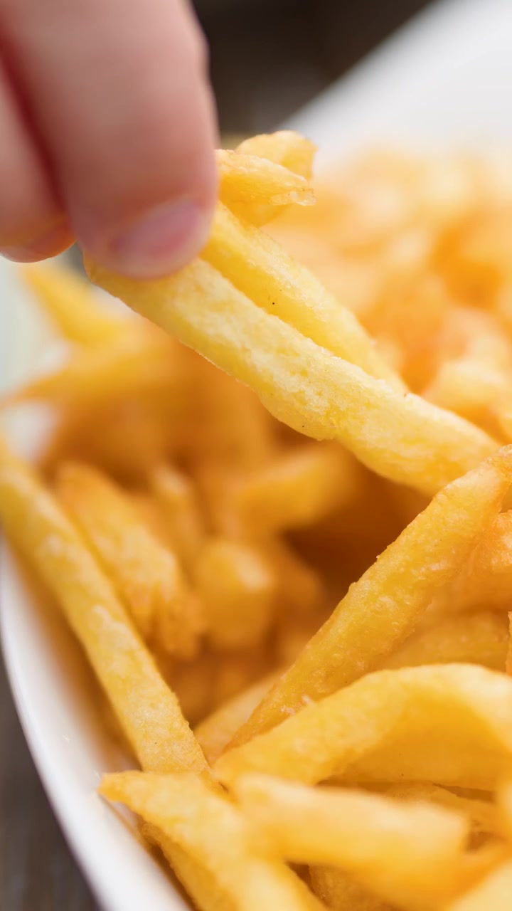 Hand picking golden French fries in natural light, shallow depth of field, static shot