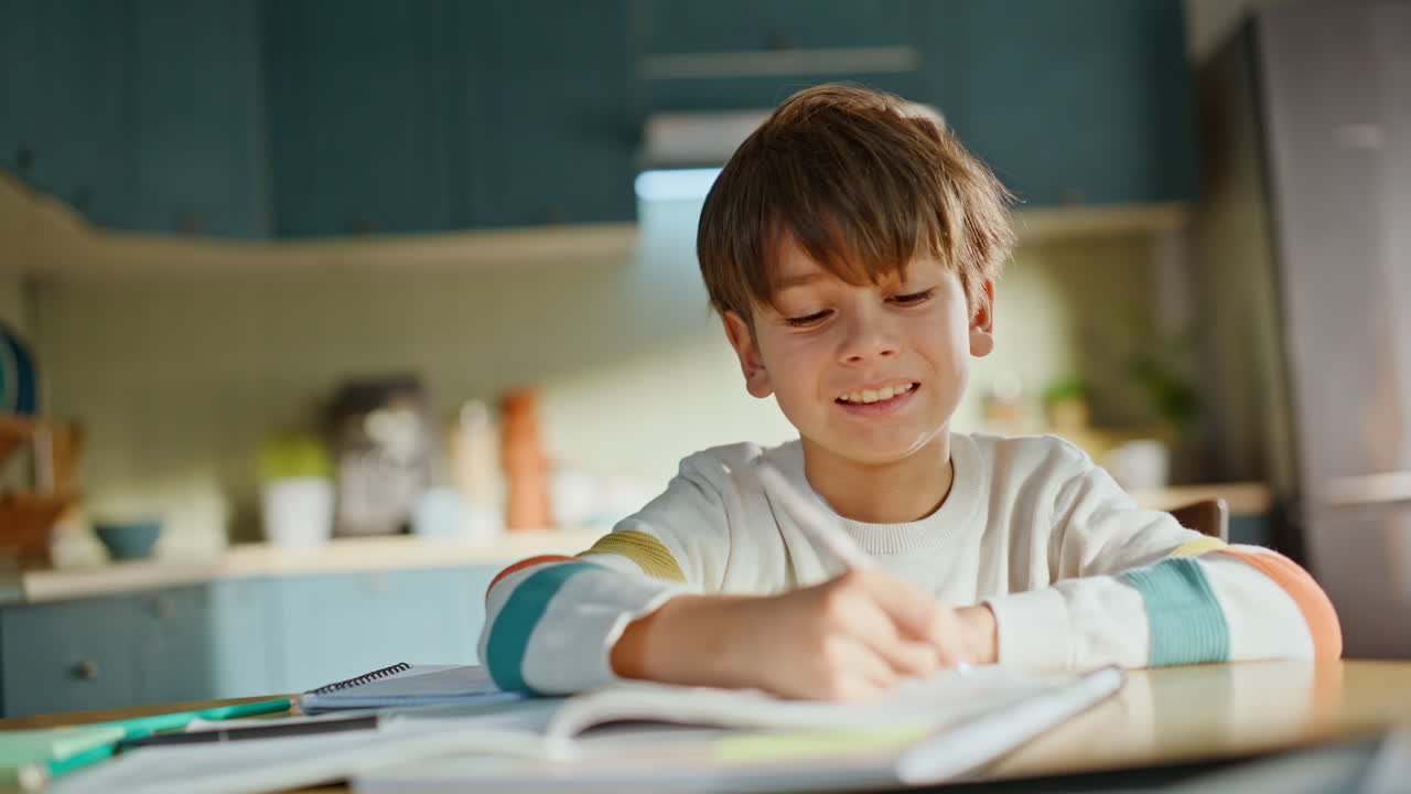 Alunno sorridente che fa i compiti, seduto al tavolo della cucina, primo piano.