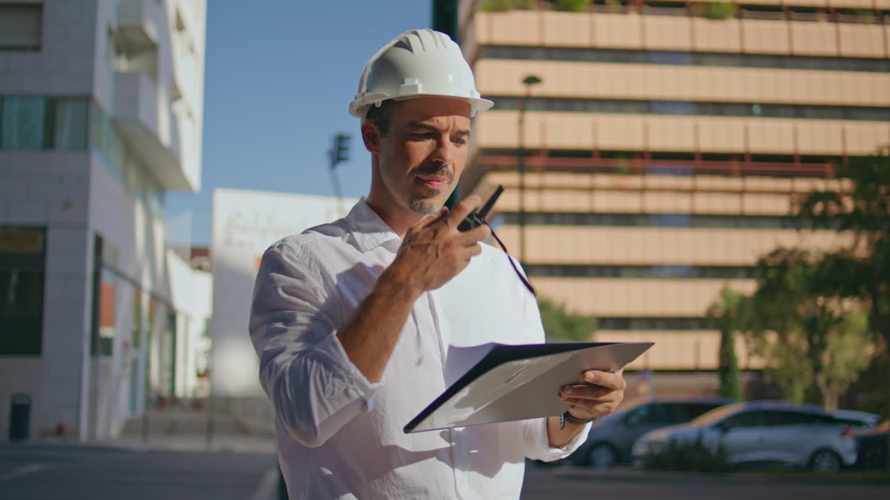 Hardhat builder talking walkie-talkie examining plan at sunlight city closeup