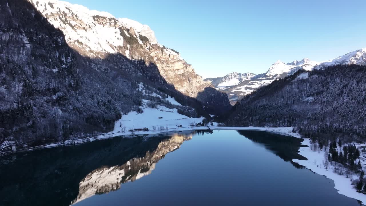 Aerial view of the Klöntalersee in Switzerland during winter. The reflection of the mountains in the still water adds another dimension to the scene, creating a perfect mirror effect.