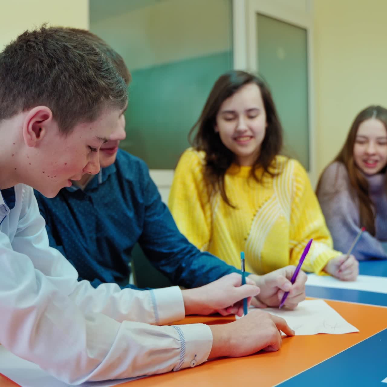 Happy children at school. Students writing joyfully during studying. Female teacher and teenage pupils in the classroom. Positive emotions at the lesson.