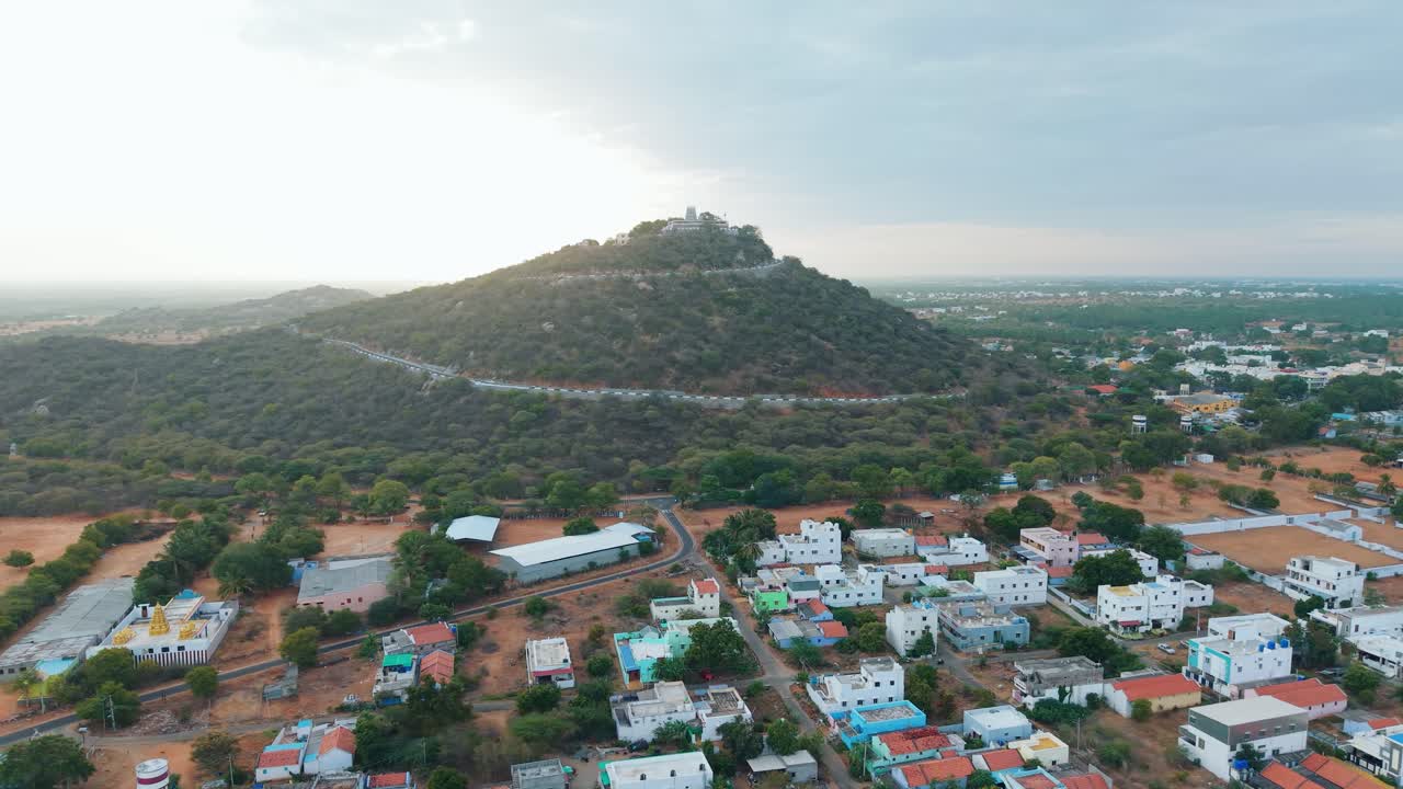 A breathtaking aerial view of a hilltop temple at sunrise, with golden rays illuminating the lush greenery, winding road, colorful houses, and serene surroundings, creating a captivating travel scene