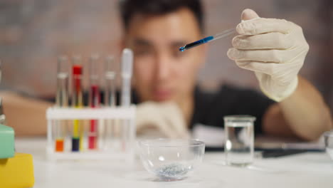 el empleado deja caer líquido azul oscuro en un cuenco con cristales en el laboratorio.